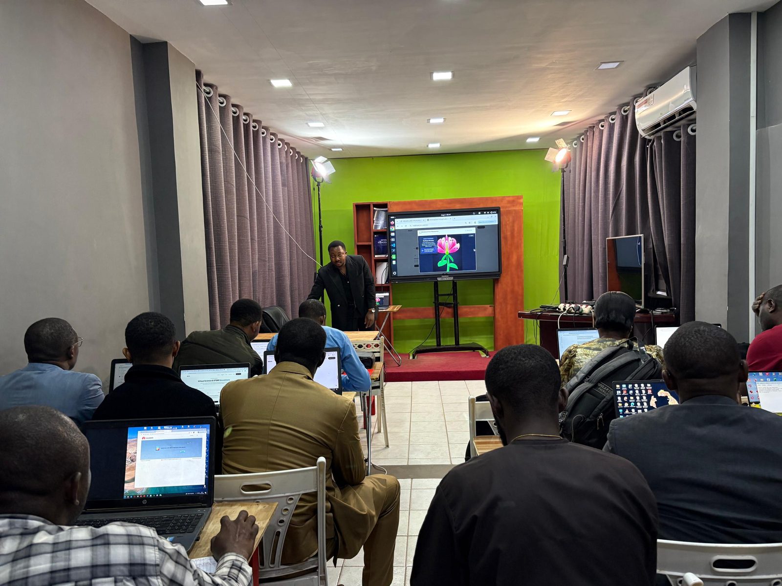 A training room. A flower simulation is on the screen, and participants work on laptops.
